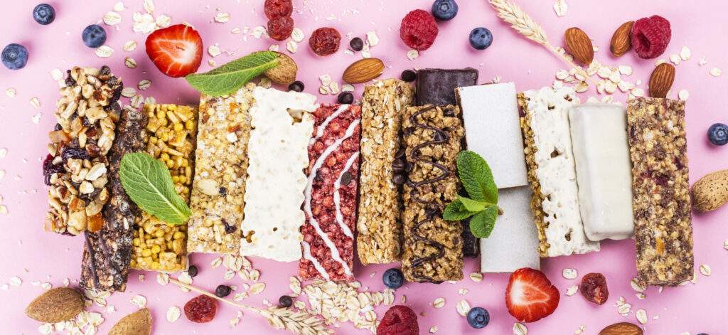 Assortment of different granola cereal bars on pink background. Healthy snacks with fruits